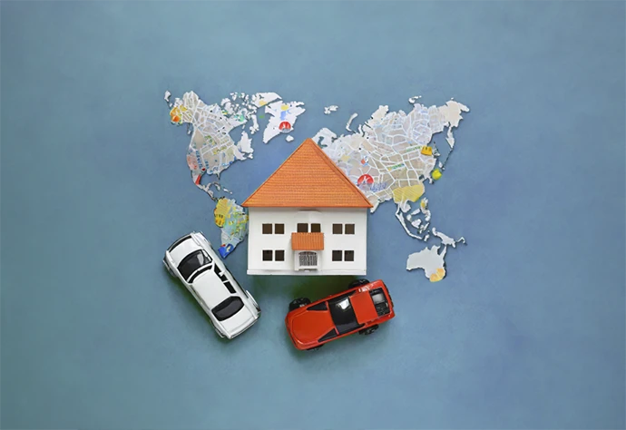 Miniature house on top of a world map and two miniature cars