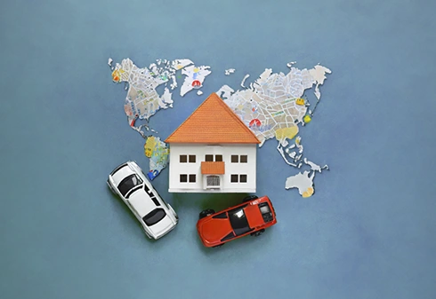 Miniature house on top of a world map and two miniature cars
