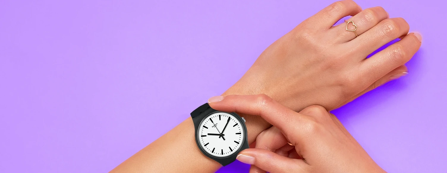 close-up of a hand adjusting the Swatch watch on the wrist, against a purple background