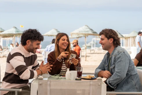 José Condessa e mais dois atores, a representar as personagens Sara Guimarães e Filipe Ribeiro, a conversarem num bar de praia