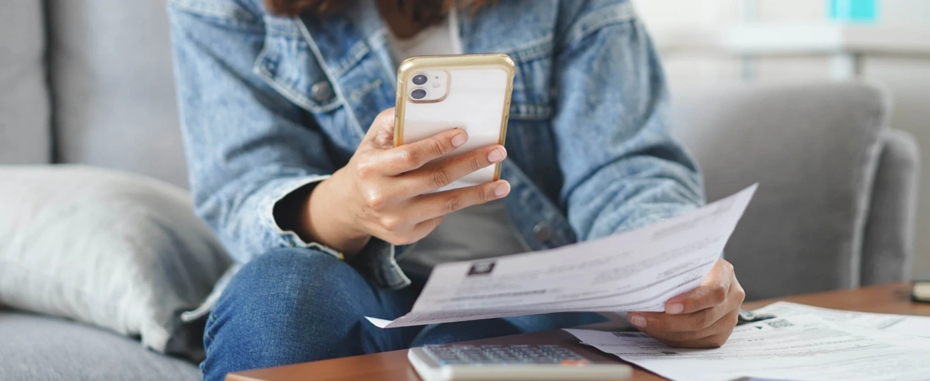 Pessoa a consultar um extrato em papel enquanto faz contas no telemóvel