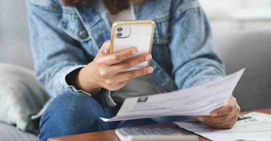 Pessoa a consultar um extrato em papel enquanto faz contas no telemóvel