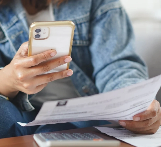 Pessoa a consultar um extrato em papel enquanto faz contas no telemóvel