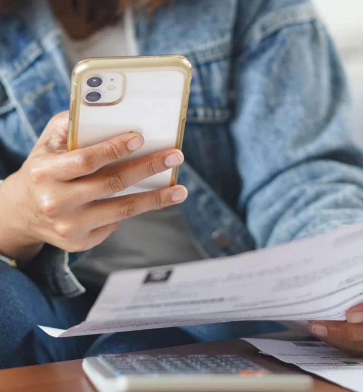 Pessoa a consultar um extrato em papel enquanto faz contas no telemóvel
