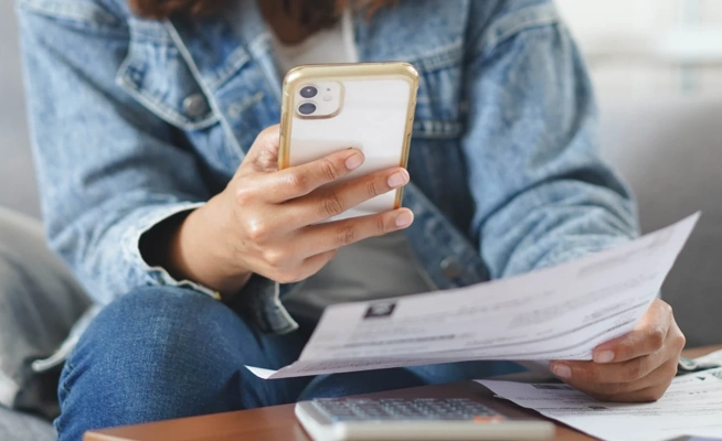 Pessoa a consultar um extrato em papel enquanto faz contas no telemóvel