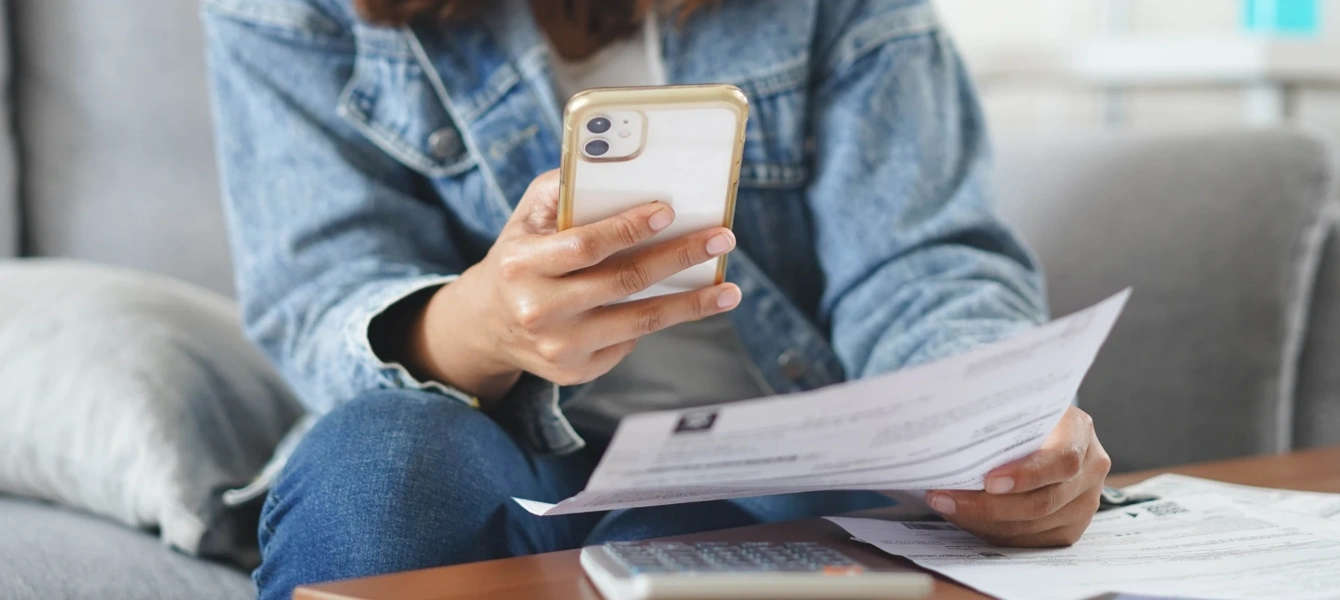 Pessoa a consultar um extrato em papel enquanto faz contas no telemóvel