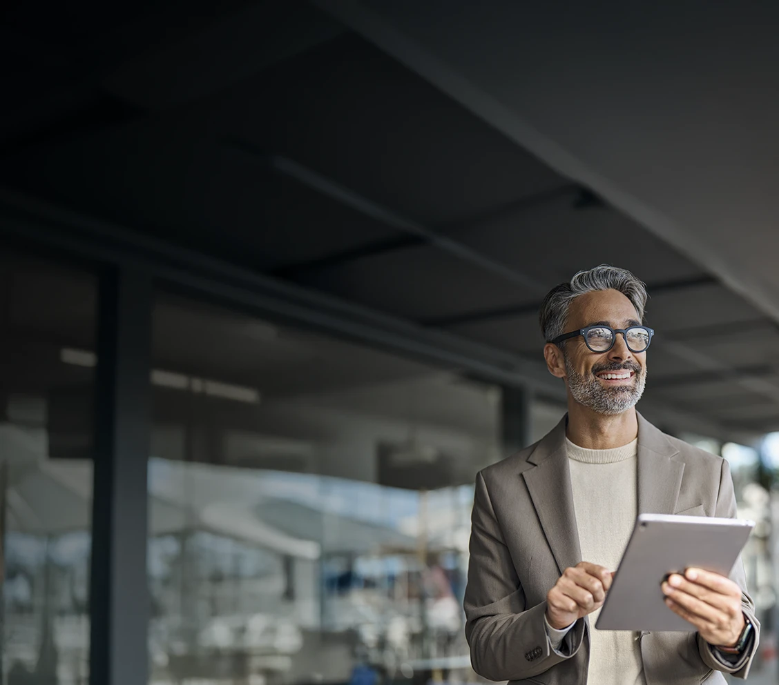 Grey-haired man with glasses, outside a building, holding a tablet