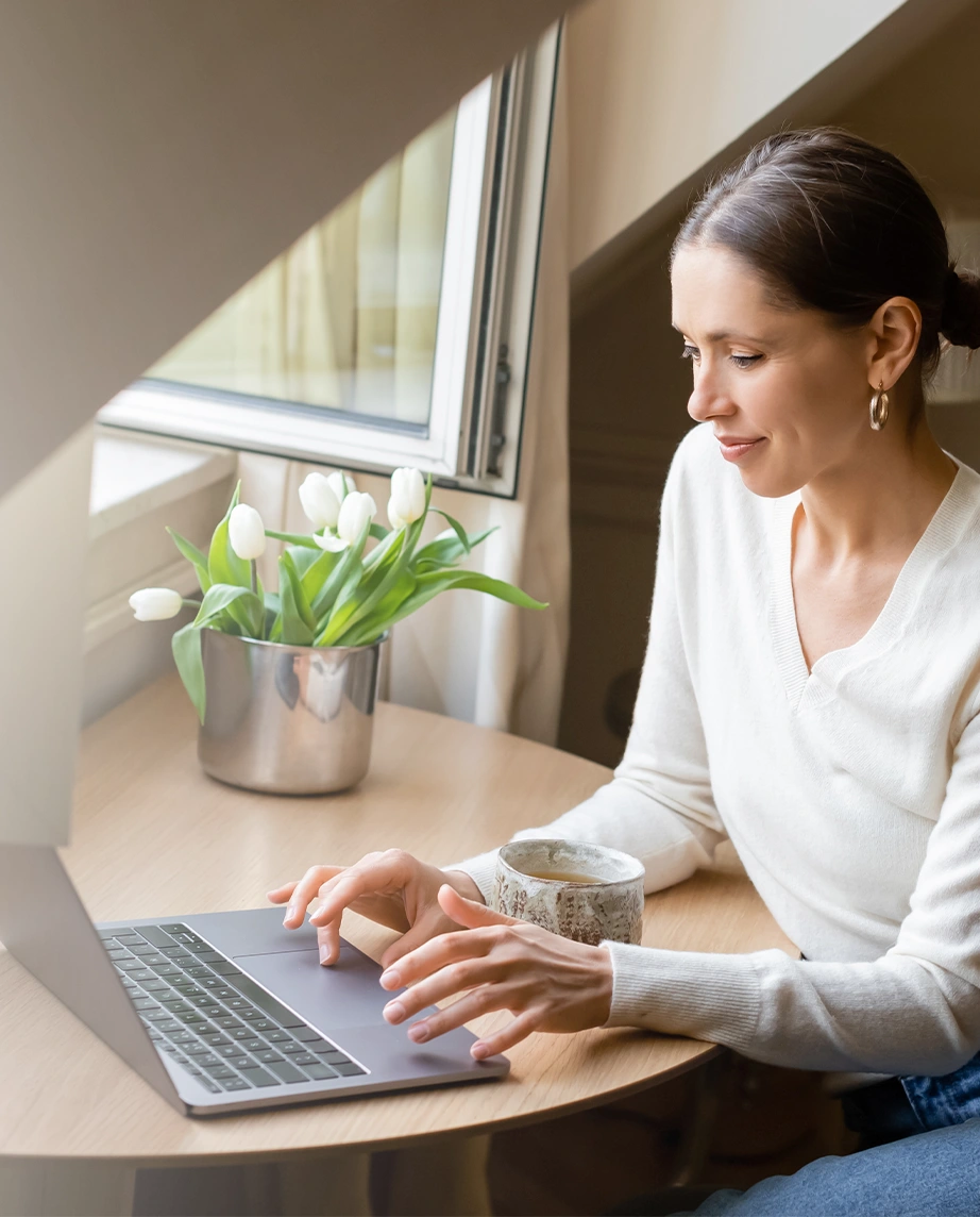 mulher sentada numa secretária à janela, a trabalhar no computador