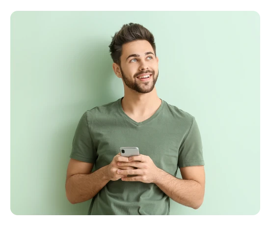 Rapaz com uma camisola verde em pé a olhar para o ar e com um telemóvel nas mãos