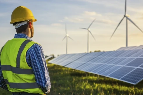 Worker observing a renewable energy field with solar panels and wind turbines