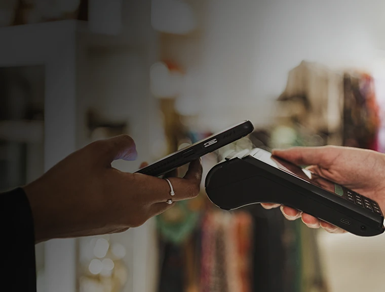 mão de comerciante a segurar TPA e mão de cliente com telemóvel a fazer pagamento