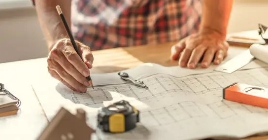 Arquiteto a desenhar numa planta de construção com ferramentas