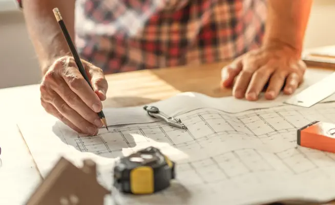 Arquiteto a desenhar numa planta de construção com ferramentas