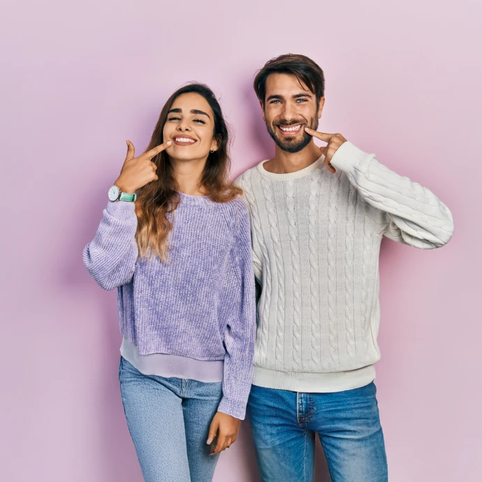 Casal sorridente aponta para os dentes, destacando saúde e estética dental