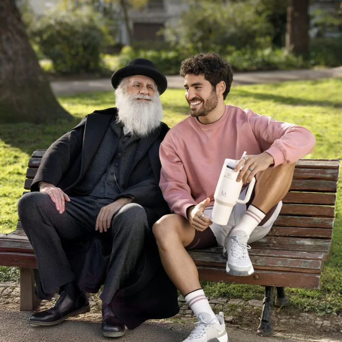 José Condessa, com uma caneca Stanley na mão, e o 'Charles Darwin' (ator) sentados num banco de jardim