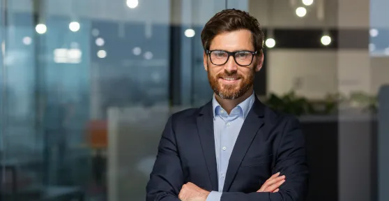 Homem com óculos, vestido com uma camisa e blazer, de braços cruzados