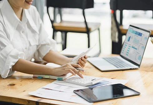 Woman smiling while managing finances at a desk with a laptop, calculator, and documents