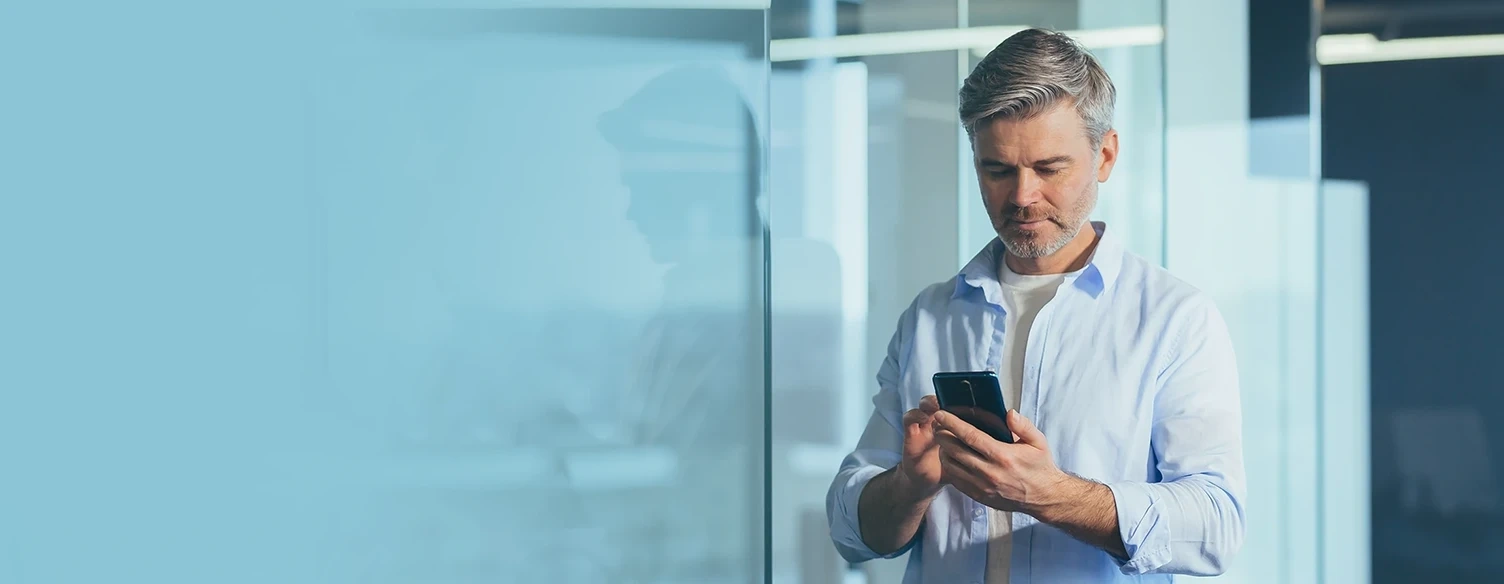 Man in a blue shirt using his mobile phone in an office environment with a blueish background