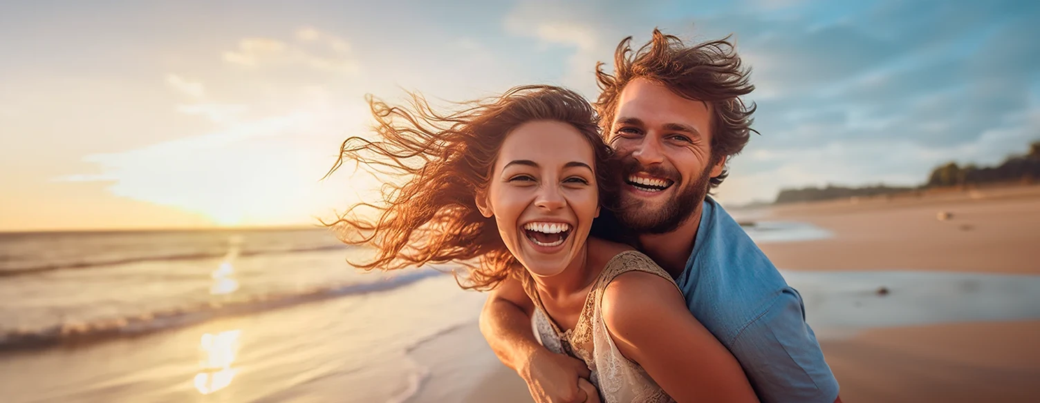 casal sorridente, abraçado, na praia ao pôr do sol