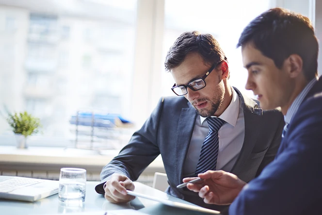 2 formally dressed men in a meeting with papers