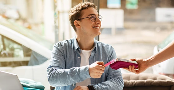 homem sorridente a pagar conta com cartão contactless num TPA