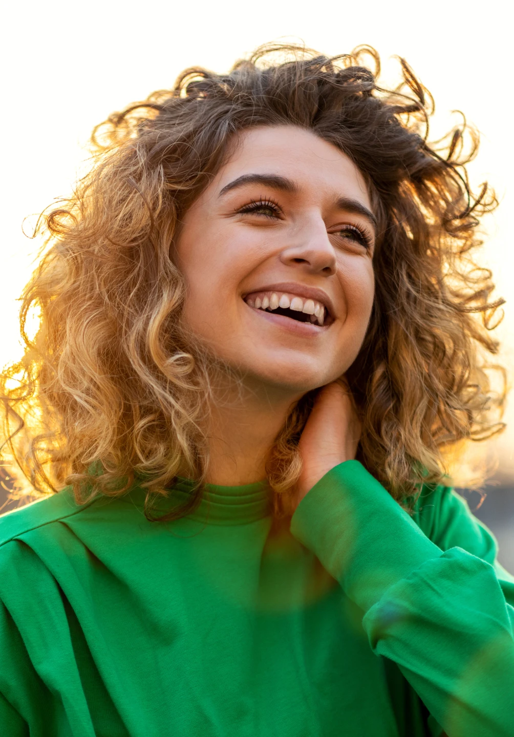 Rapariga com uma camisola verde a sorrir no pôr do sol