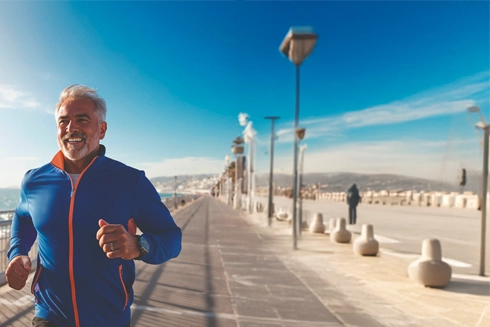 Middle-aged man smiling and jogging along the beach