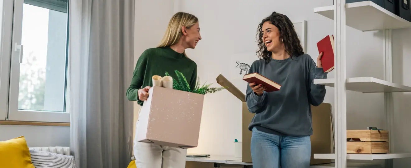 Duas amigas sorridentes a arrumar livros e objetos numa estante
