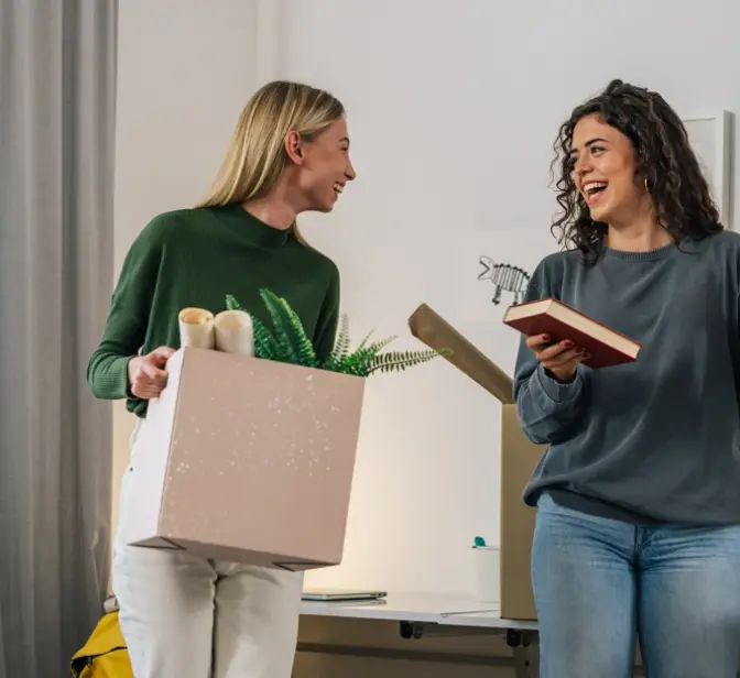 Duas amigas sorridentes a arrumar livros e objetos numa estante