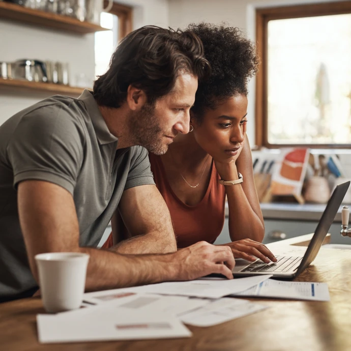 Casal concentrado a consultar documentos e um portátil na cozinha, planeando finanças