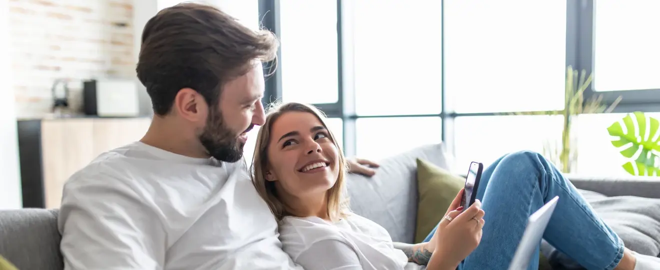Casal no sofá, mulher a olhar para o homem enquanto segura o telemóvel