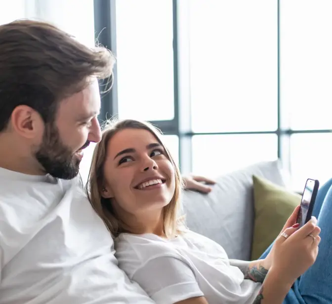 Casal no sofá, mulher a olhar para o homem enquanto segura o telemóvel