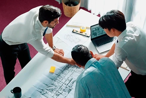 Três arquitetos a analisar plantas de um projeto numa mesa