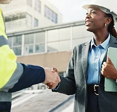 Woman in a suit and hard hat shakes hands with a worker on a building site
