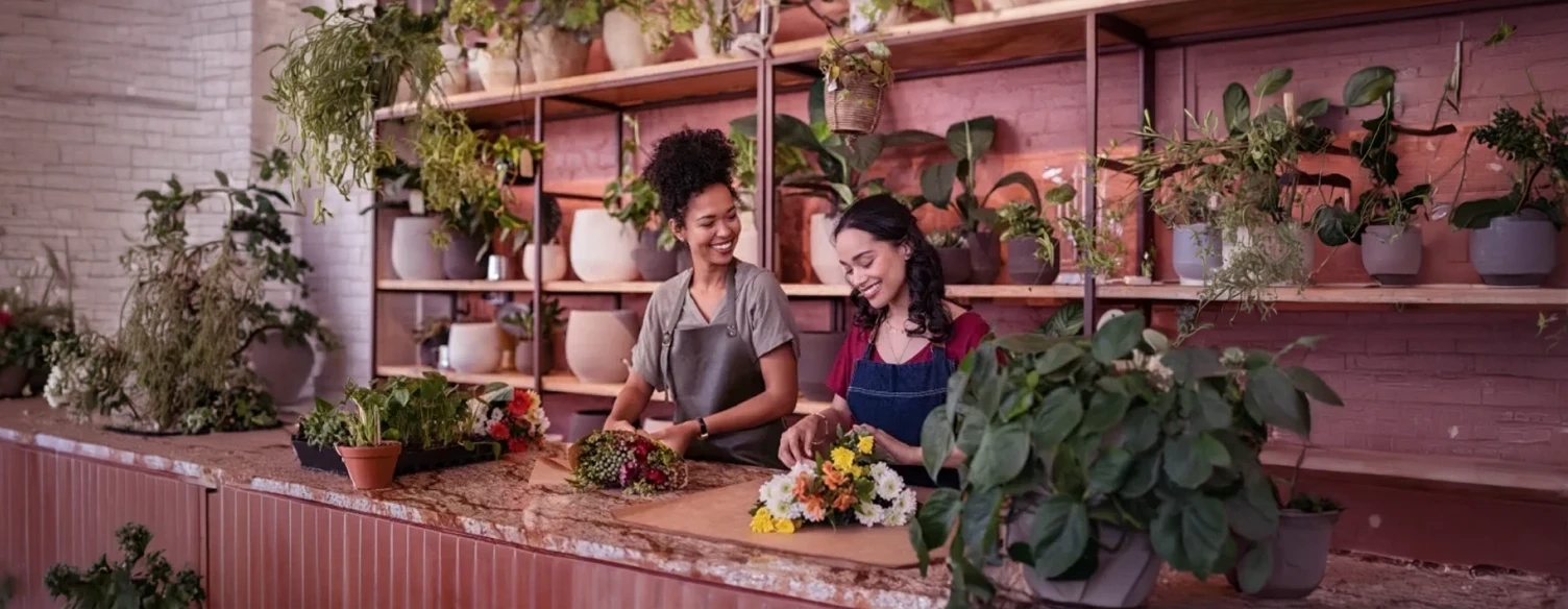 Duas floristas sorridentes a arranjar flores ao balcão de uma loja