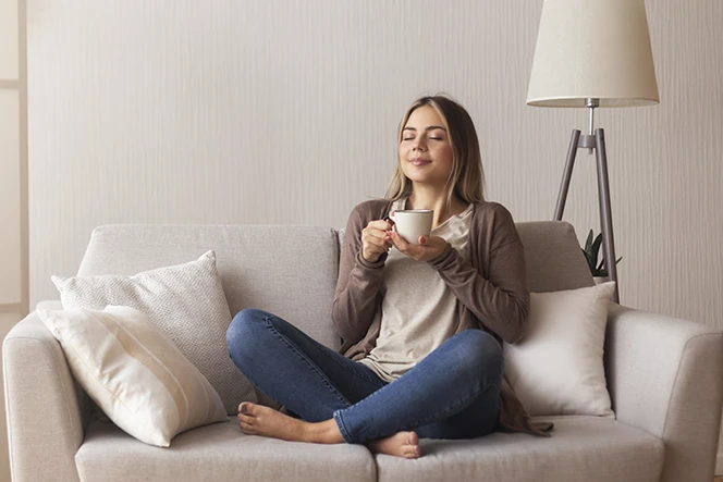senhora sentada no sofá com pernas cruzadas e chávena na mão, com ar tranquilo
