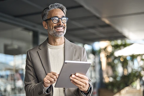 grey-haired man with glasses, outside a building, holding a tablet