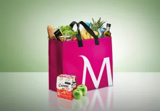 Saco de compras cerise, com o "M" de Millennium bcp desenhado, cheio de fruta, legumes e outra comida