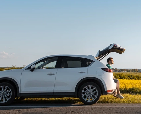  white car parked on the roadside, with the trunk open and a man sitting inside