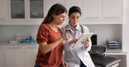 Médica a mostrar informação a uma paciente num tablet