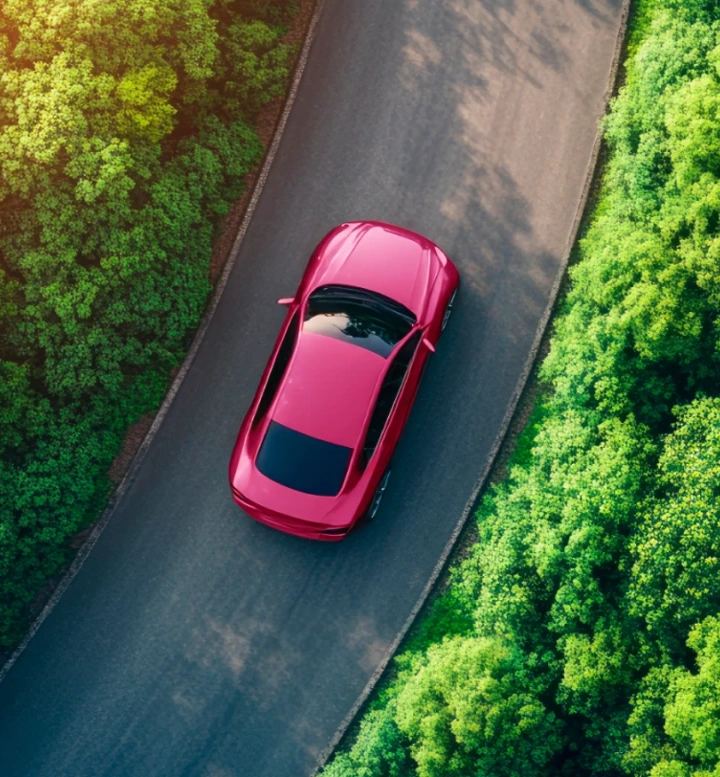 Vista aérea de um carro cor-de-rosa escuro a circular numa estrada rodeada por uma floresta verde