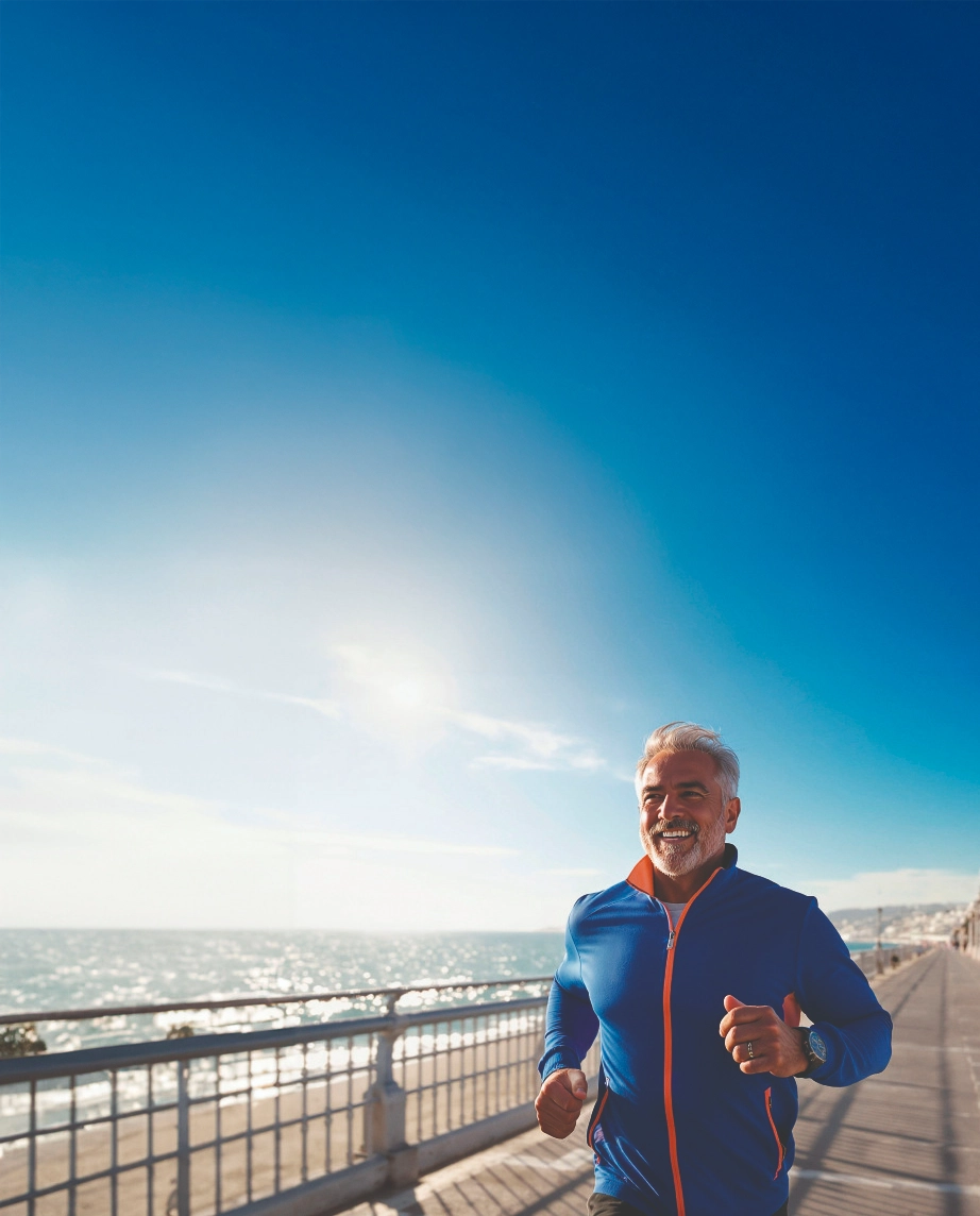 Middle-aged man smiling and jogging along the beach
