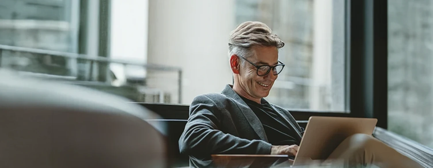 Homem de óculos a sorrir enquanto trabalha num portátil num espaço de escritório moderno