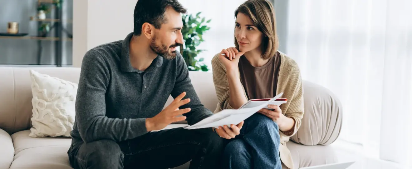 Casal a discutir documentos no sofá, homem a gesticular