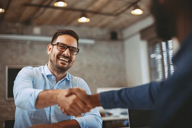 Smiling man with glasses shaking hands with another person in an office