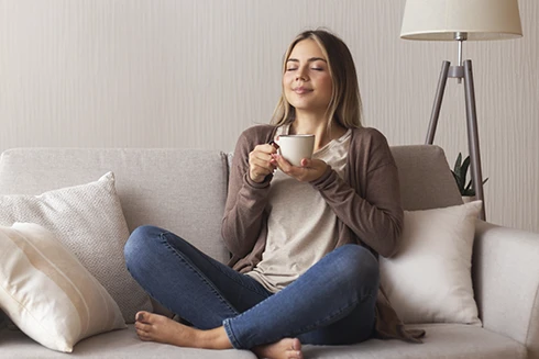 woman sitting cross-legged on the sofa, holding a cup, with a calm expression
