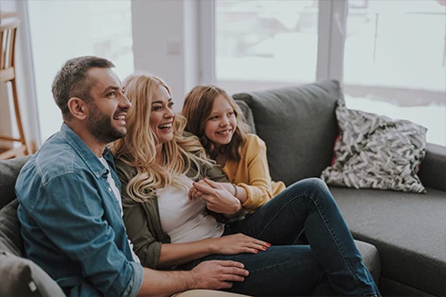 casal e filha pequena sorridentes, num sofá, num momento de cumplicidade