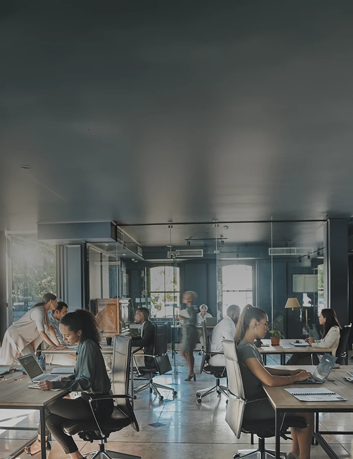 Equipa trabalha num escritório moderno e luminoso, colaborando em diferentes tarefas com computadores e reuniões