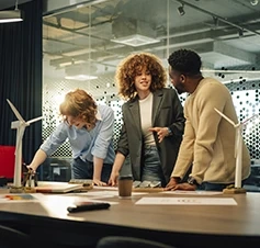 Three colleagues discuss a renewable energy project with wind turbine models