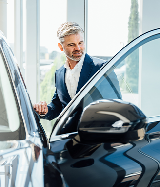 gentleman at the car dealership, with a car door open, observing it